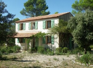 A two-story building with a tiled roof and green shutters, surrounded by trees and shrubs. - Country house in Provence (PONTEVES)