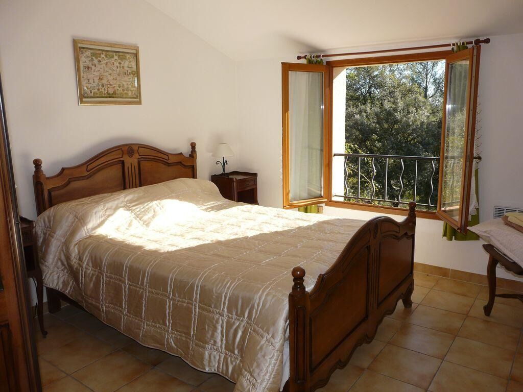 Ein Schlafzimmer mit einem großen Bett, einem Nachttisch, einem Fenster mit Blick auf Bäume und einem gerahmten Bild an der Wand.