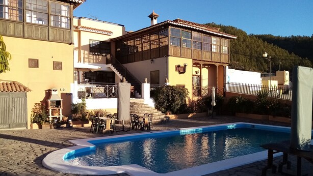 A pool area with a stone patio, outdoor seating, and a building with a balcony and stairs.