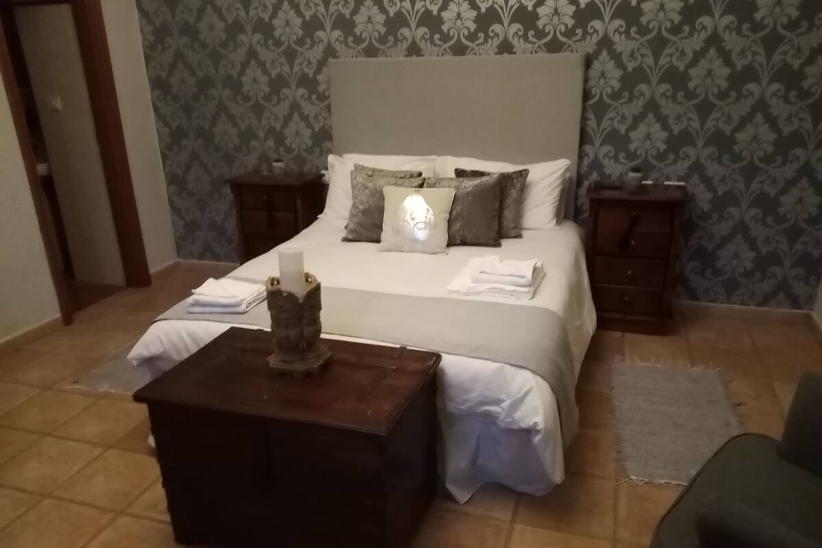 Ein Schlafzimmer mit einem Bett, Nachttischen, einem Beistelltisch und einem dekorativen Gegenstand.