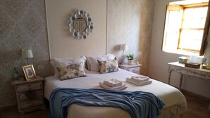A bedroom with a bed, pillows, a nightstand, a lamp, a window, and a wall decoration.