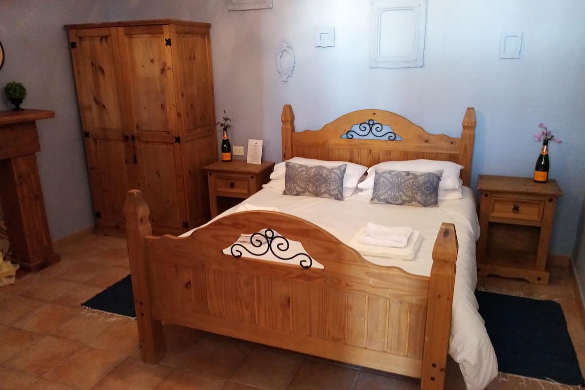 Ein hölzernes Bett mit Kopfteil, zwei Nachttische, ein Schrank und ein kleiner Tisch mit einer Flasche und einer Speisekarte.