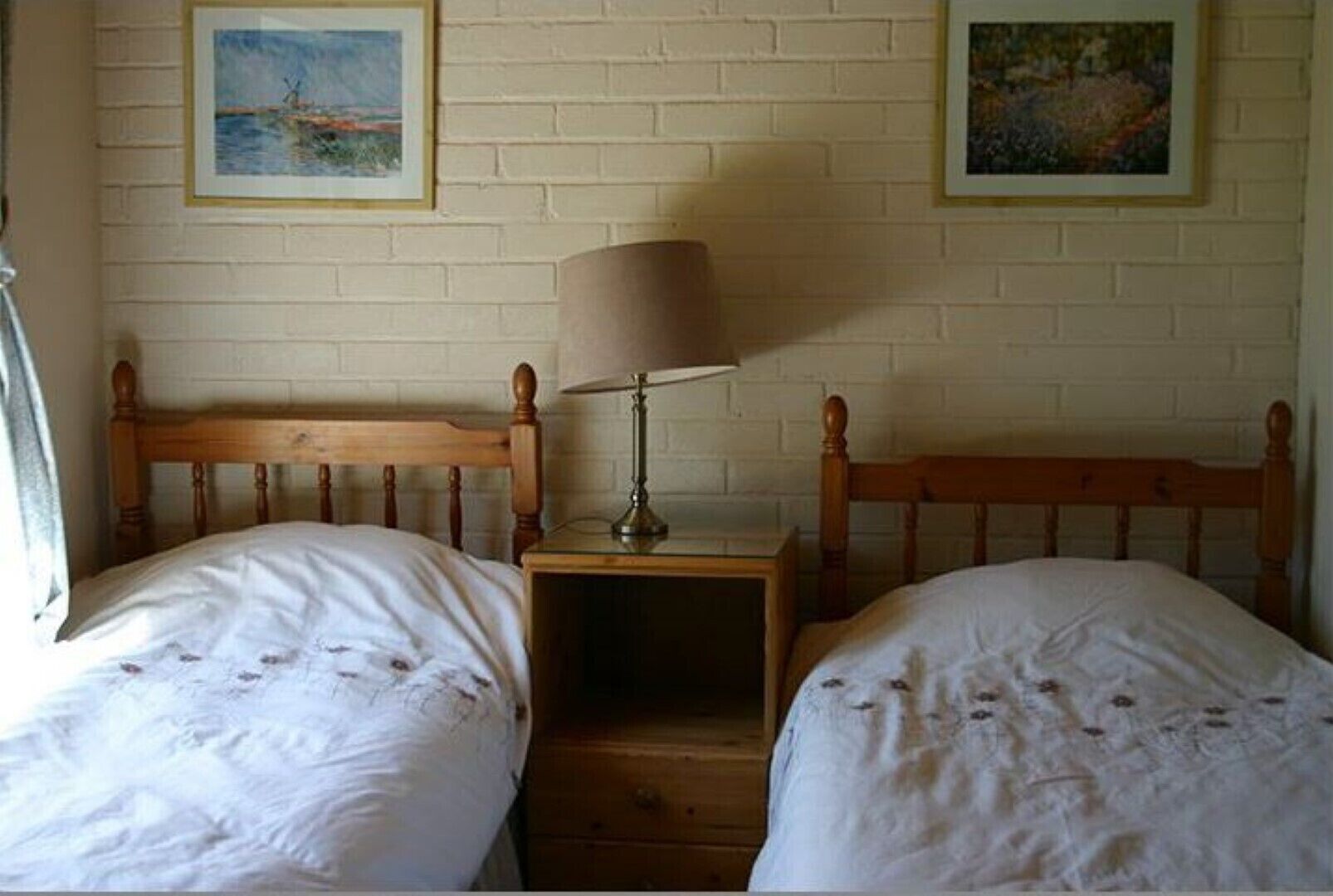 Ein Zimmer mit zwei Holzbetten, einem Nachttisch mit Lampe und zwei gerahmten Bildern an der Wand.