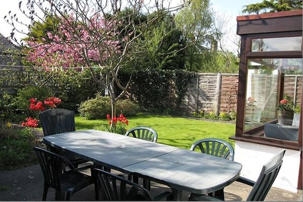 A patio with a table and chairs, surrounded by a garden with flowering plants and a brick wall.