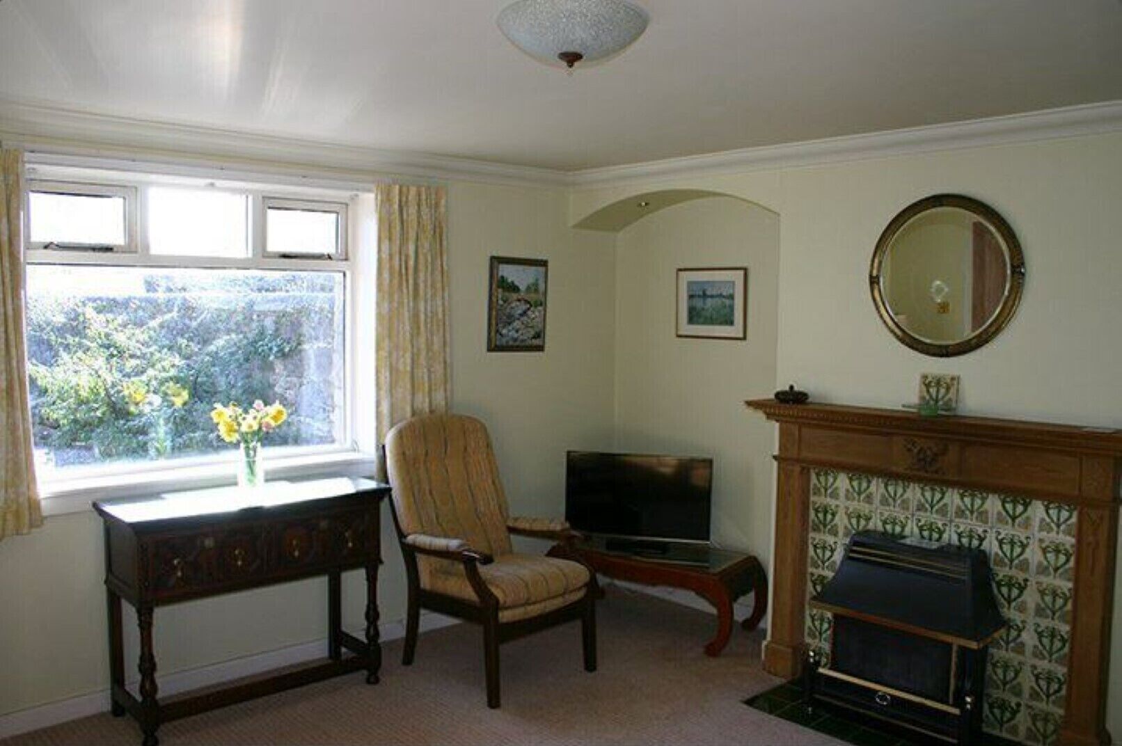 A living room with a fireplace, a television, a chair, a table, and a window with curtains.