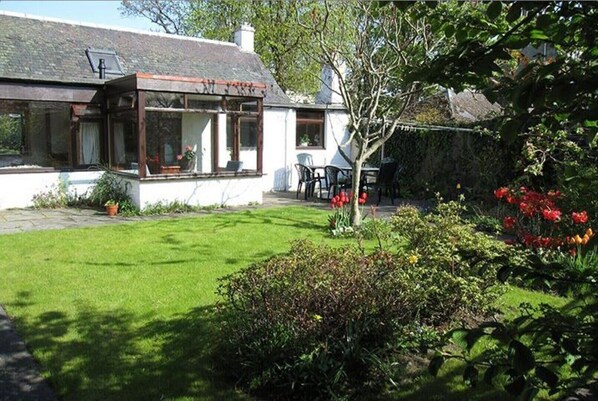 A house with a conservatory, a lawn, and a garden with flowers.