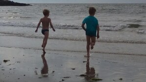 Two children walking on a wet beach with waves coming in.