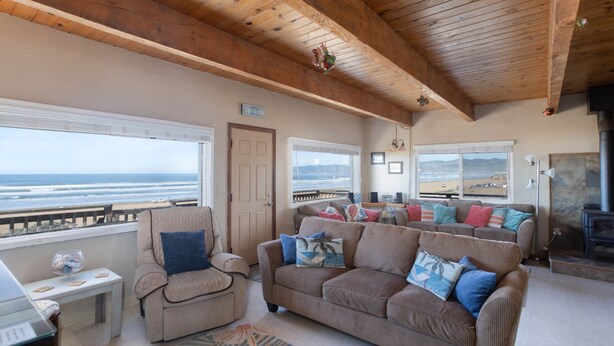 A spacious living room with a large window overlooking the ocean, a cozy seating area with a sofa and armchairs, and a fireplace. - Steps from the Sand! Spacious Beach Home with Amazing Ocean Views! (Oceano)