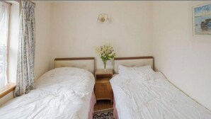 Una habitación con dos camas individuales, una mesita con un florero y un cuadro en la pared.