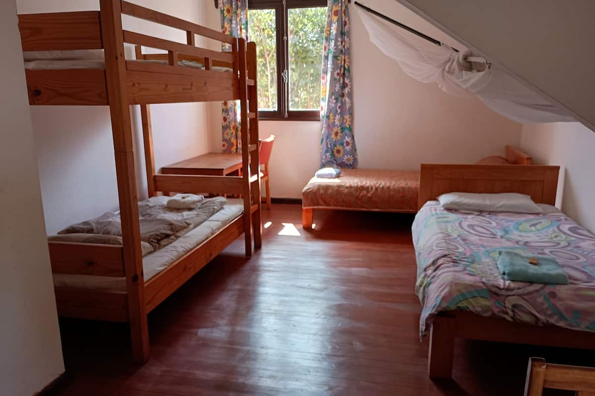 Ein Schlafsaalzimmer mit drei Etagenbetten, einem Holztisch und einem Stuhl.
