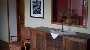 Un mobiletto in legno con cassetti, una fotografia in bianco e nero incorniciata al muro, una sedia e un vaso con fiori sul mobiletto.