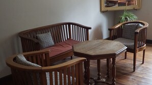Una stanza con un tavolo da pranzo in legno, due sedie in legno, un divano e uno specchio appeso al muro.