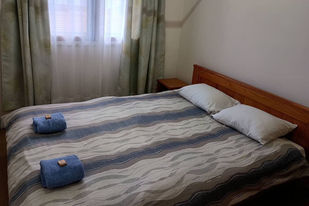 Ein ordentlich bezogenes Bett mit einem gestreiften Bettüberwurf, zwei Kissen und zwei gefalteten Handtüchern.
