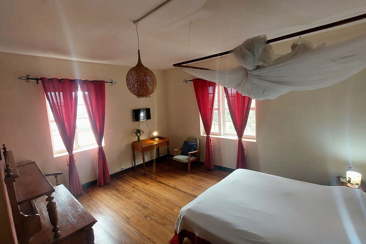 Ein Zimmer mit einem Bett, Holzmöbeln, einem Schreibtisch und roten Vorhängen.
