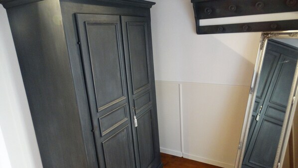 A room with a dark wooden wardrobe, a white wall, and a door with a mirror.
