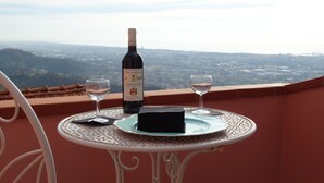 Ein Tisch mit einer Weinflasche und zwei Gläsern auf einem Balkon mit Blick auf eine Stadtlandschaft.