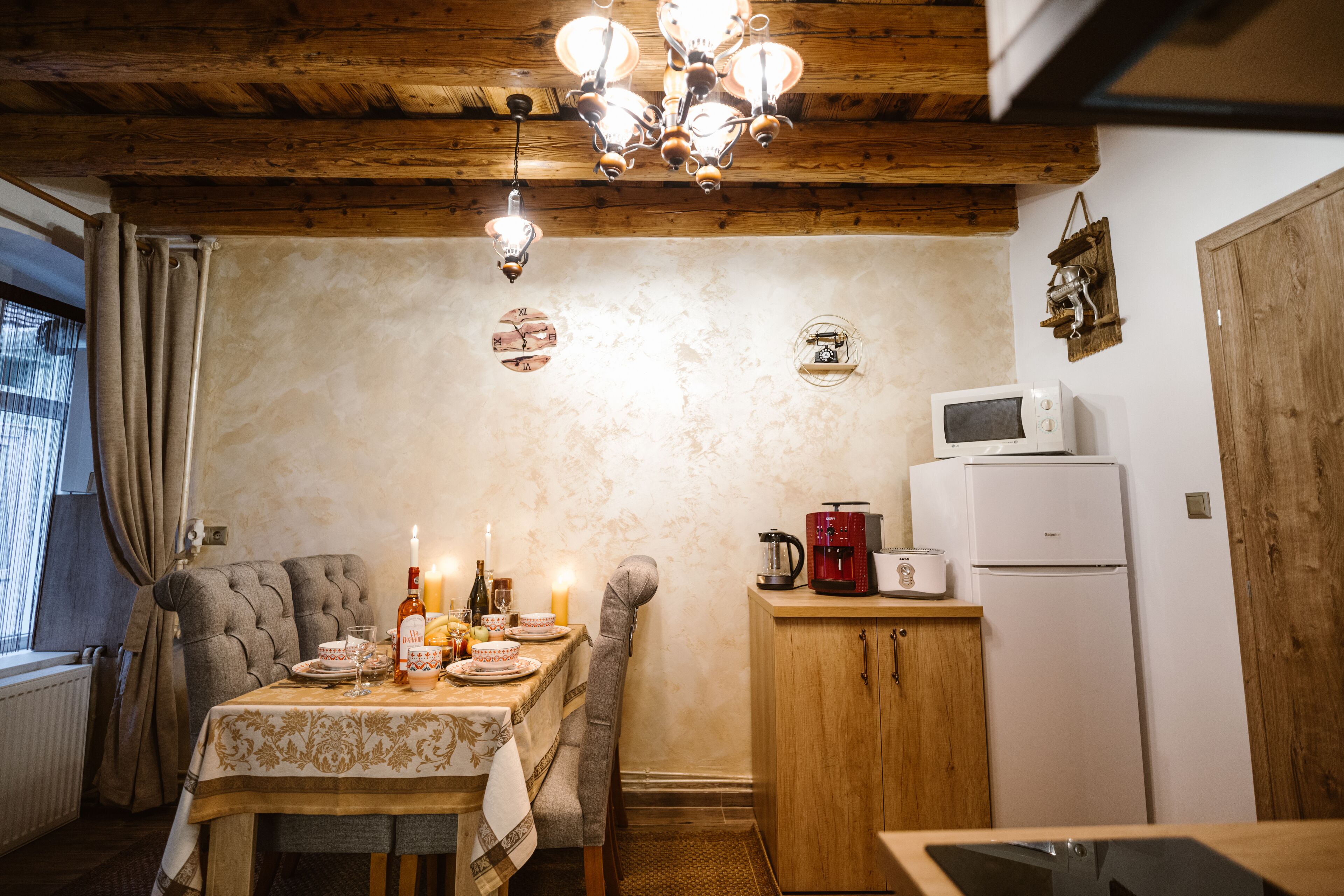 A cozy kitchen with a wooden ceiling, a dining table set for two, and a refrigerator.