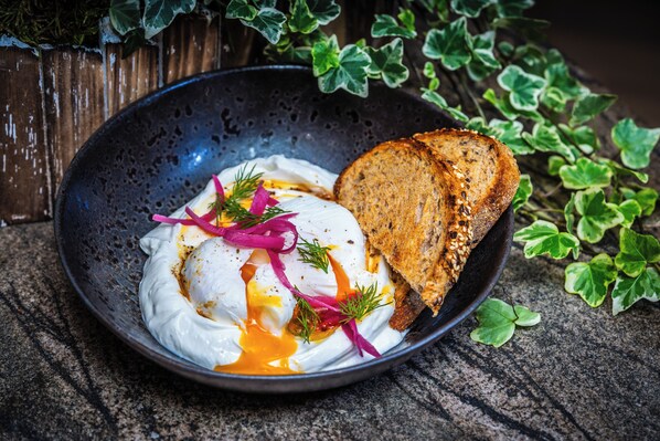 Un plat composé d’un œuf poché, de crème aigre et d’une tranche de pain grillé, le tout présenté sur une assiette foncée.