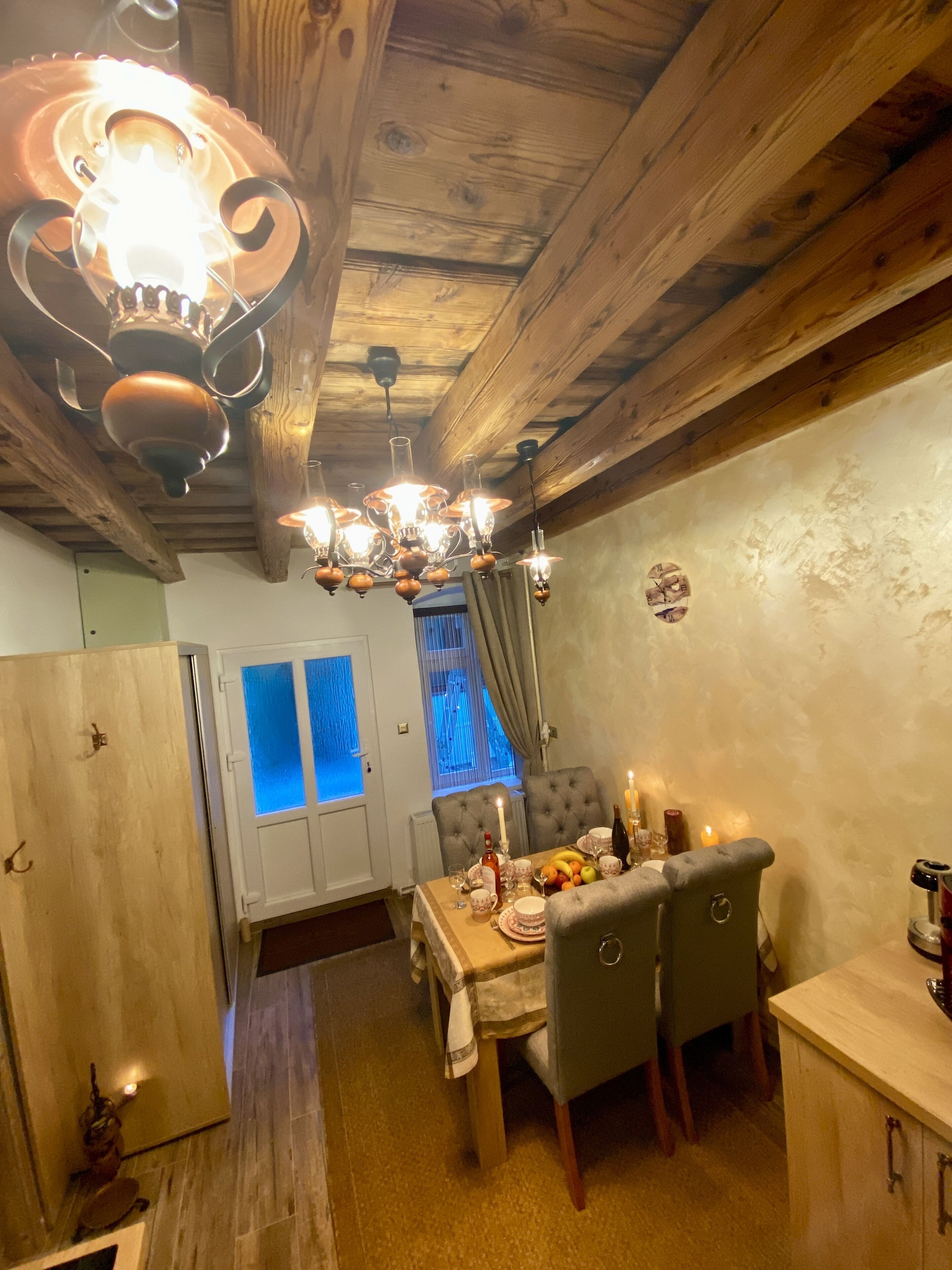 A cozy dining area with a wooden ceiling, a chandelier, and a table set for a meal.