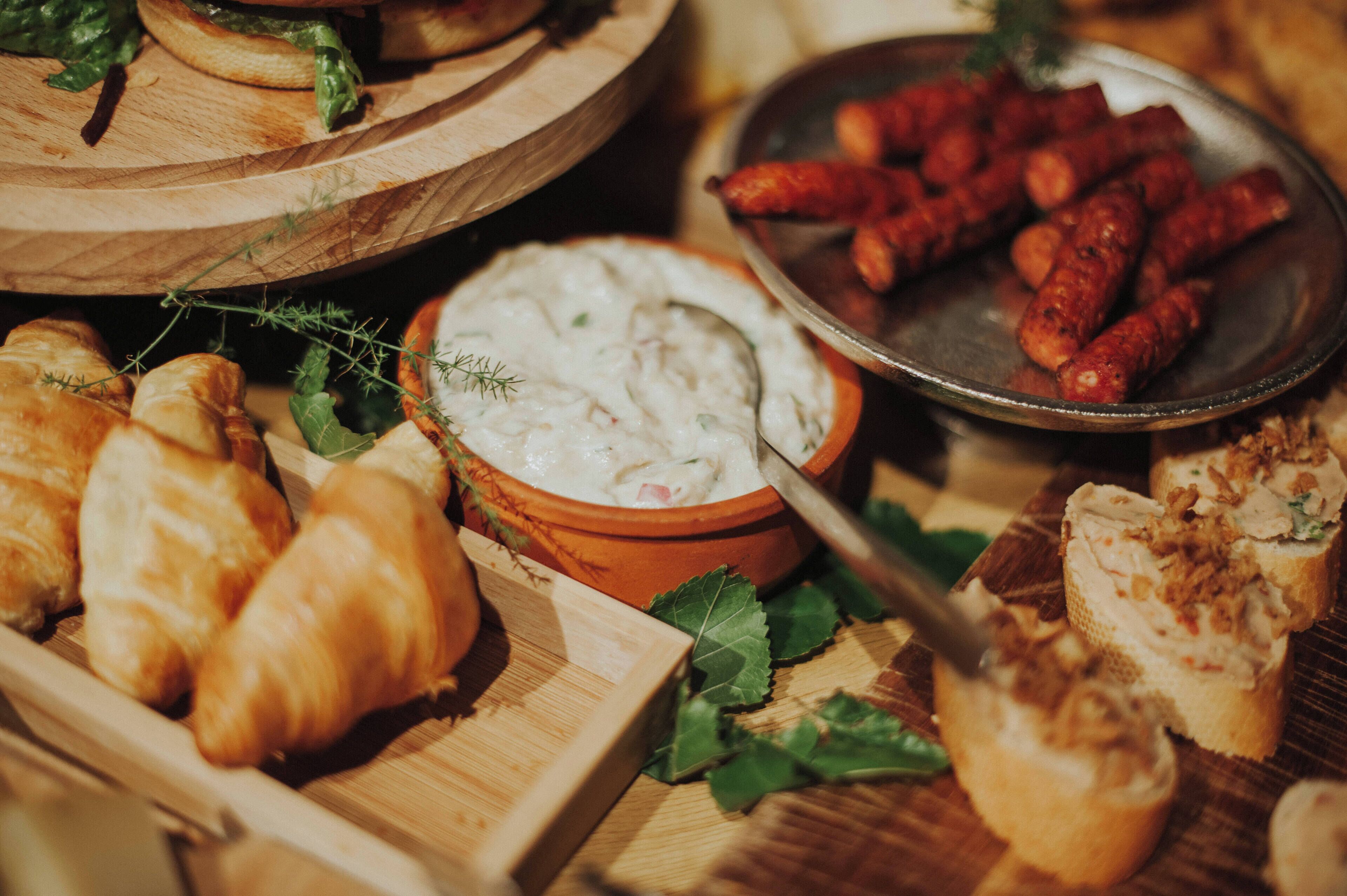 Une variété d’aliments, notamment des croissants, un bol de trempette et des saucisses, présentés sur une planche en bois.