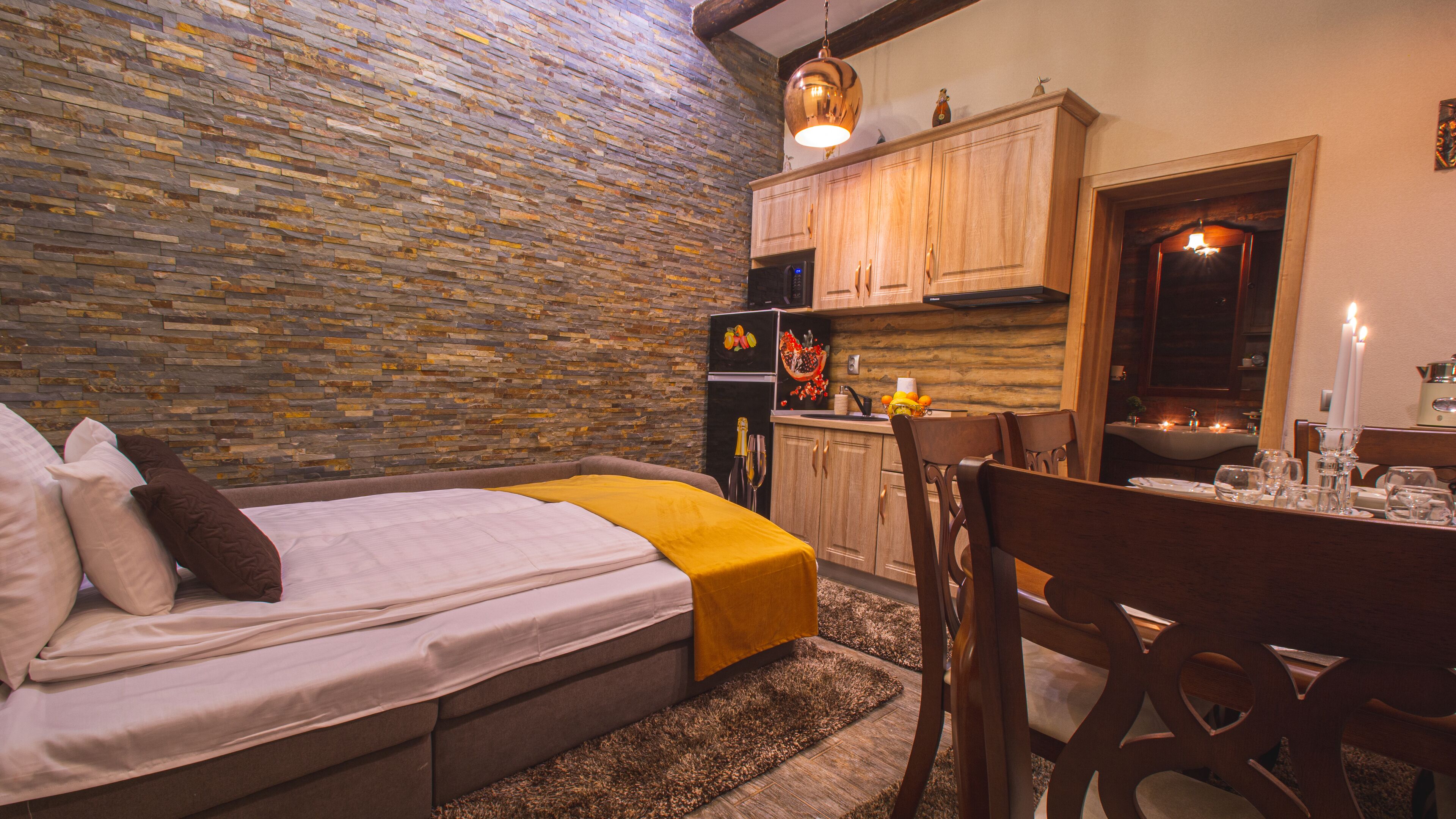 Un dormitorio acogedor con cama, una mesa de madera con sillas, una cocina con armarios de madera y una pared de piedra.