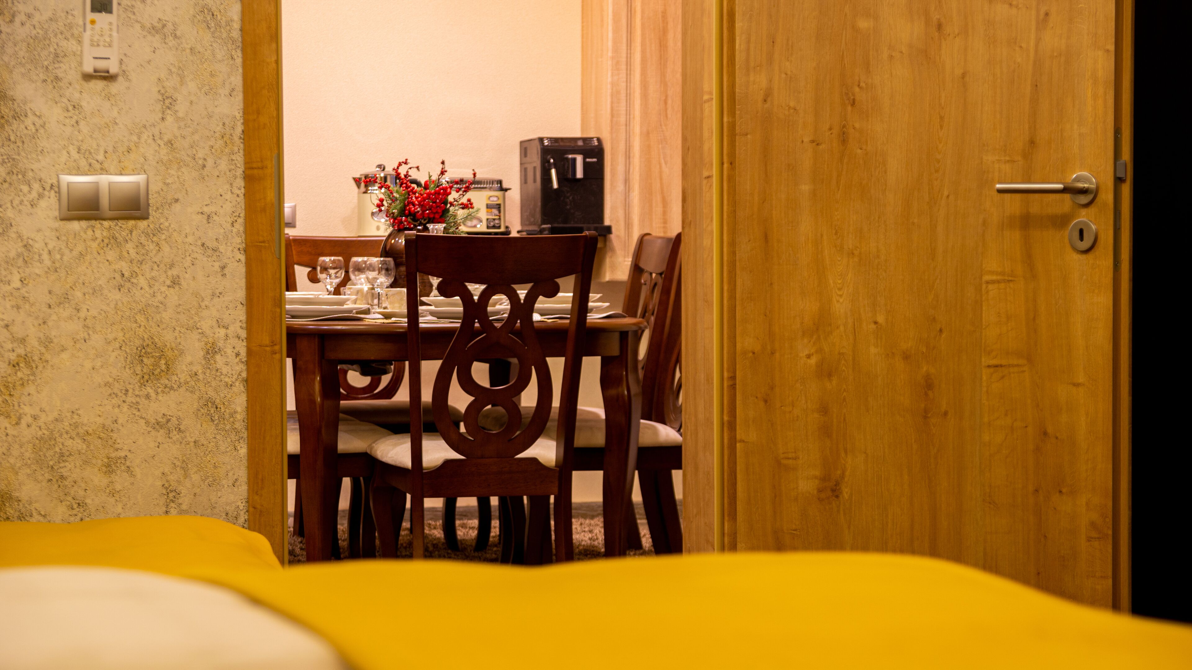 A dining area with a wooden table set for two, a coffee machine, and a vase with red berries.