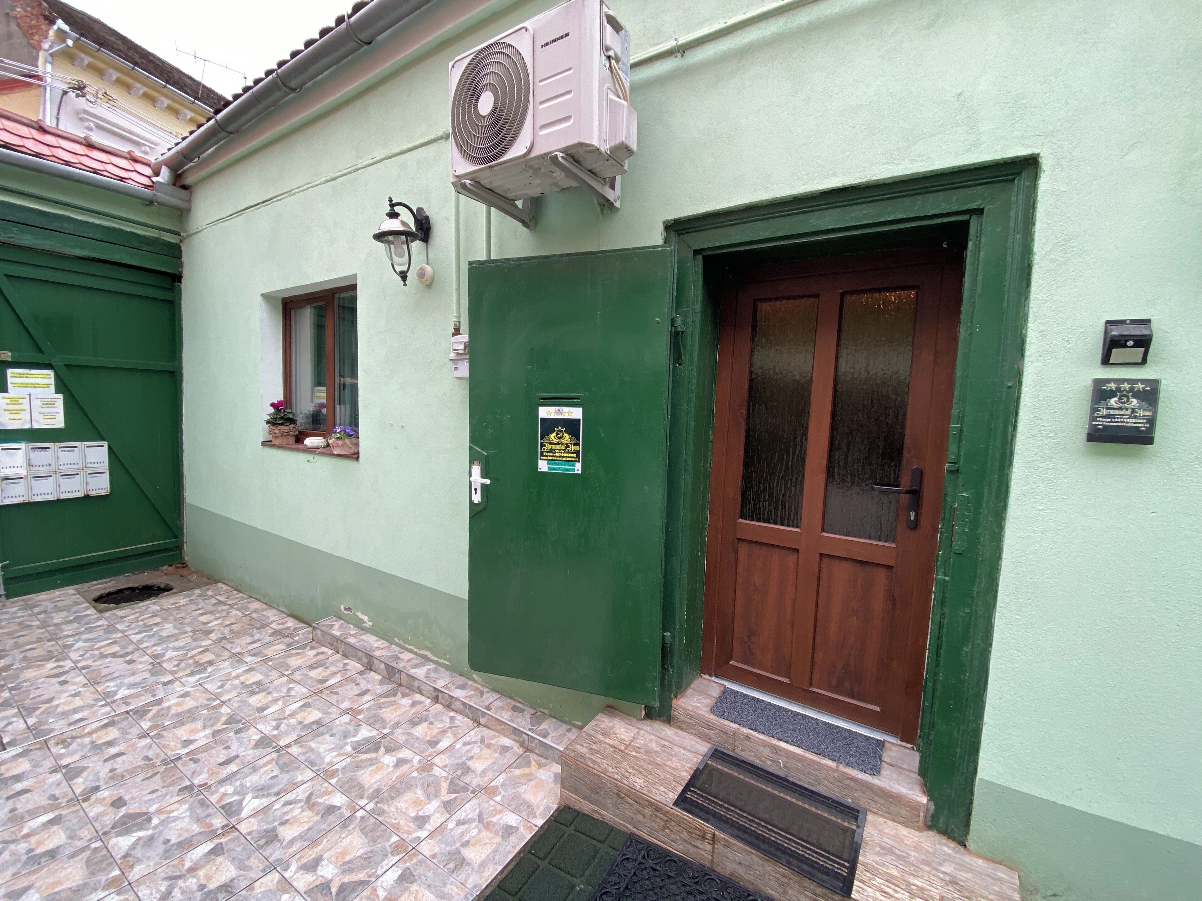 A building with a green door, a window, and a wall-mounted air conditioning unit.