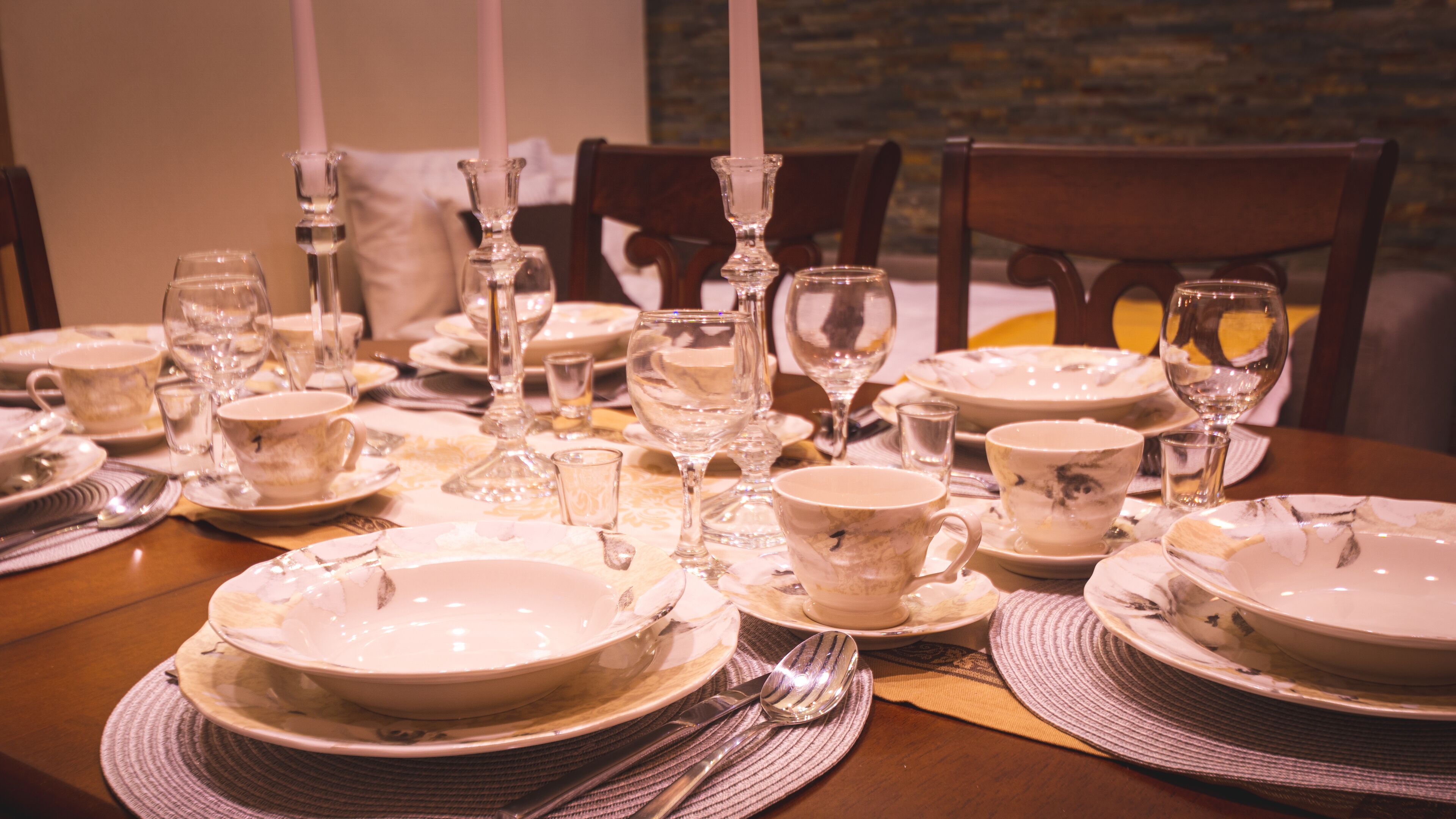 Una mesa de comedor dispuesta con platos, vasos y cubiertos, sobre individuales.