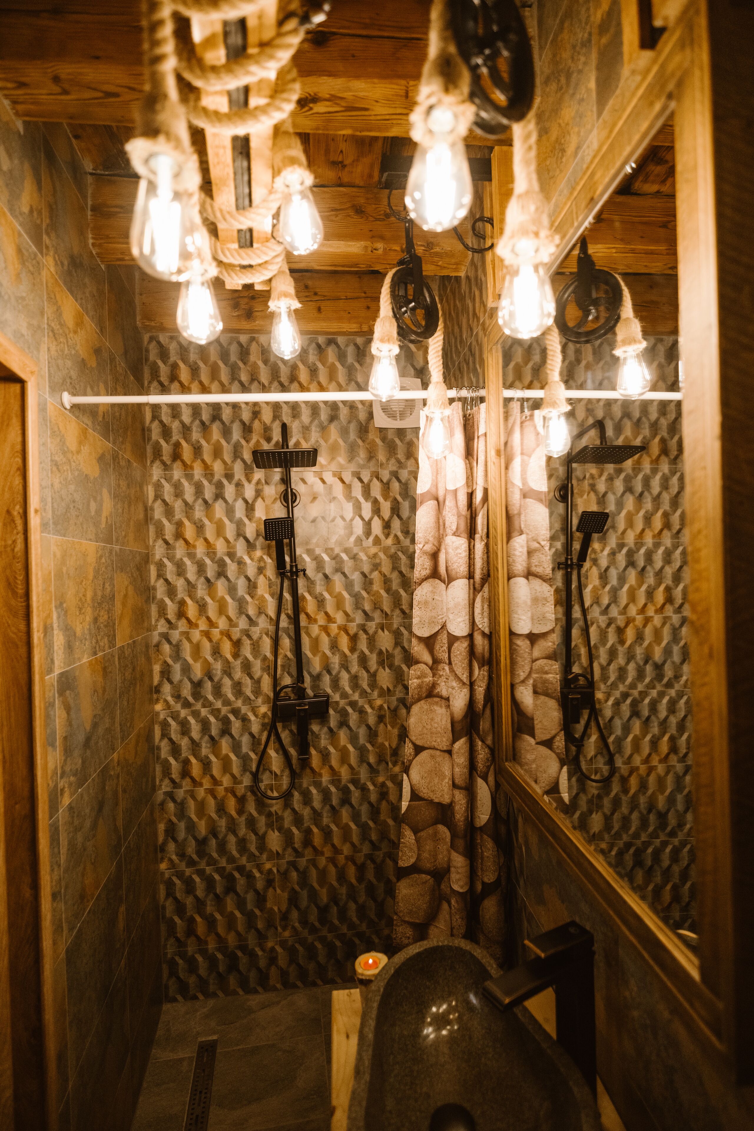 A bathroom with a stone-patterned wall, a wooden ceiling, and a mirror reflecting the light fixture.