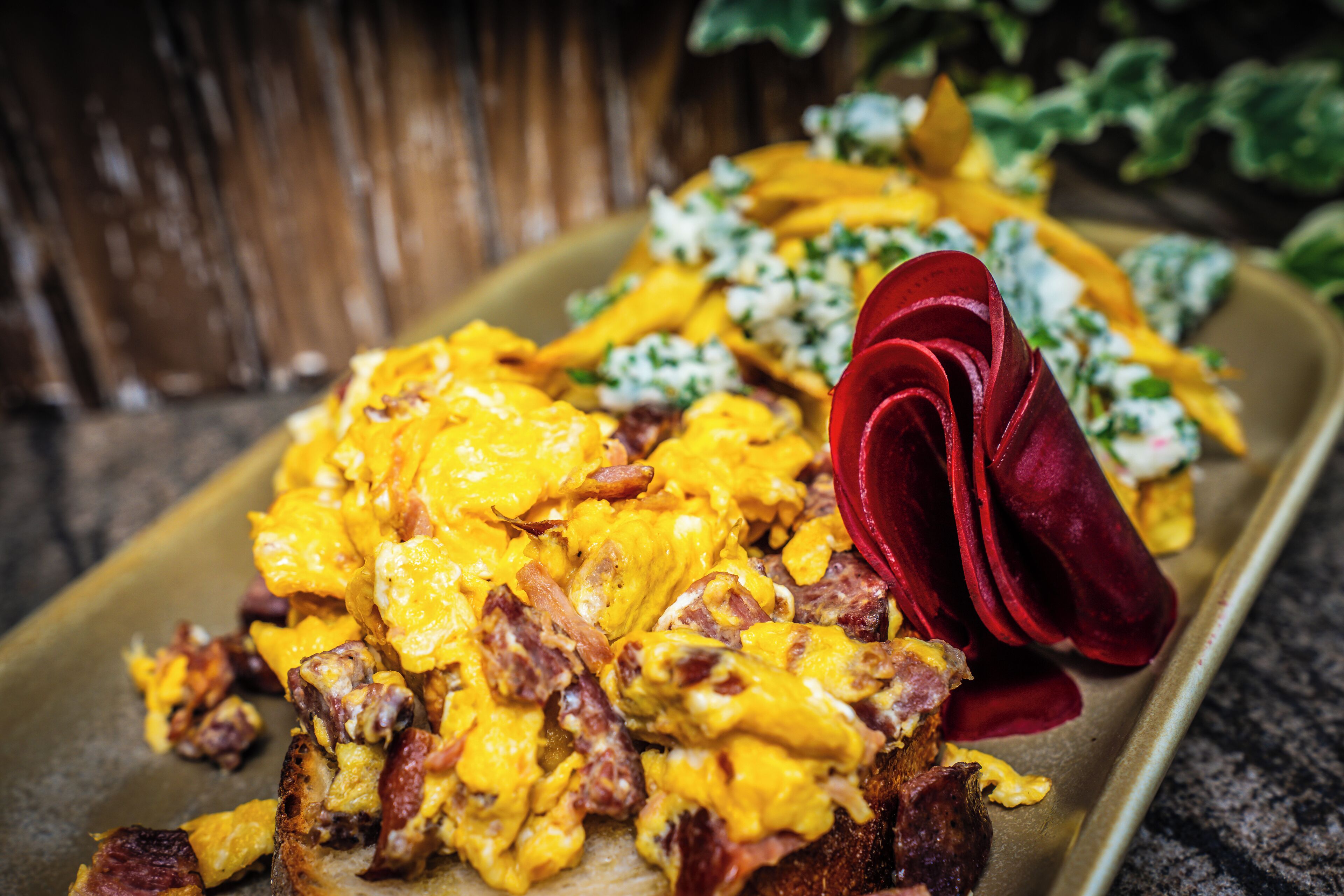 Une assiette de petit-déjeuner avec des œufs brouillés, du bacon et une rose rouge décorative.