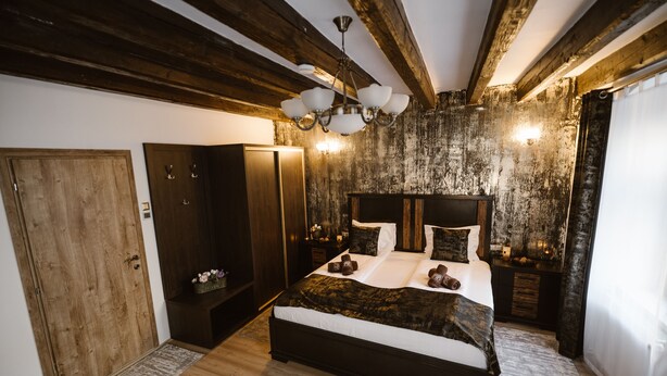 A bedroom with a wooden ceiling, a large bed, bedside tables, and a nightstand. - Hermannstadt House (Sibiu)