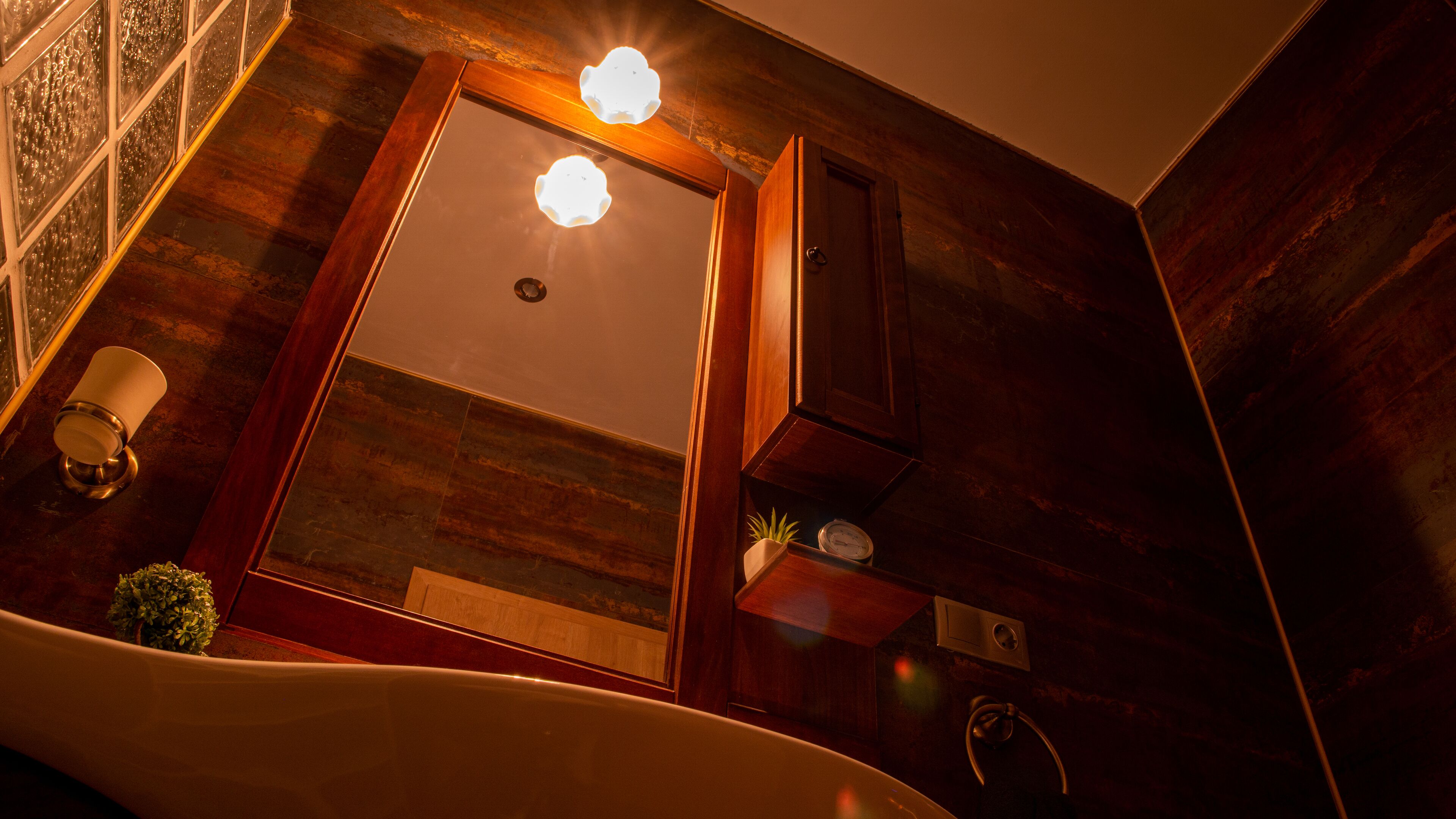 A bathroom with a wooden vanity, a mirror, a light fixture, a clock, and a plant.
