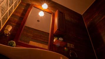 A bathroom with a wooden vanity, a mirror, a light fixture, a clock, and a plant.