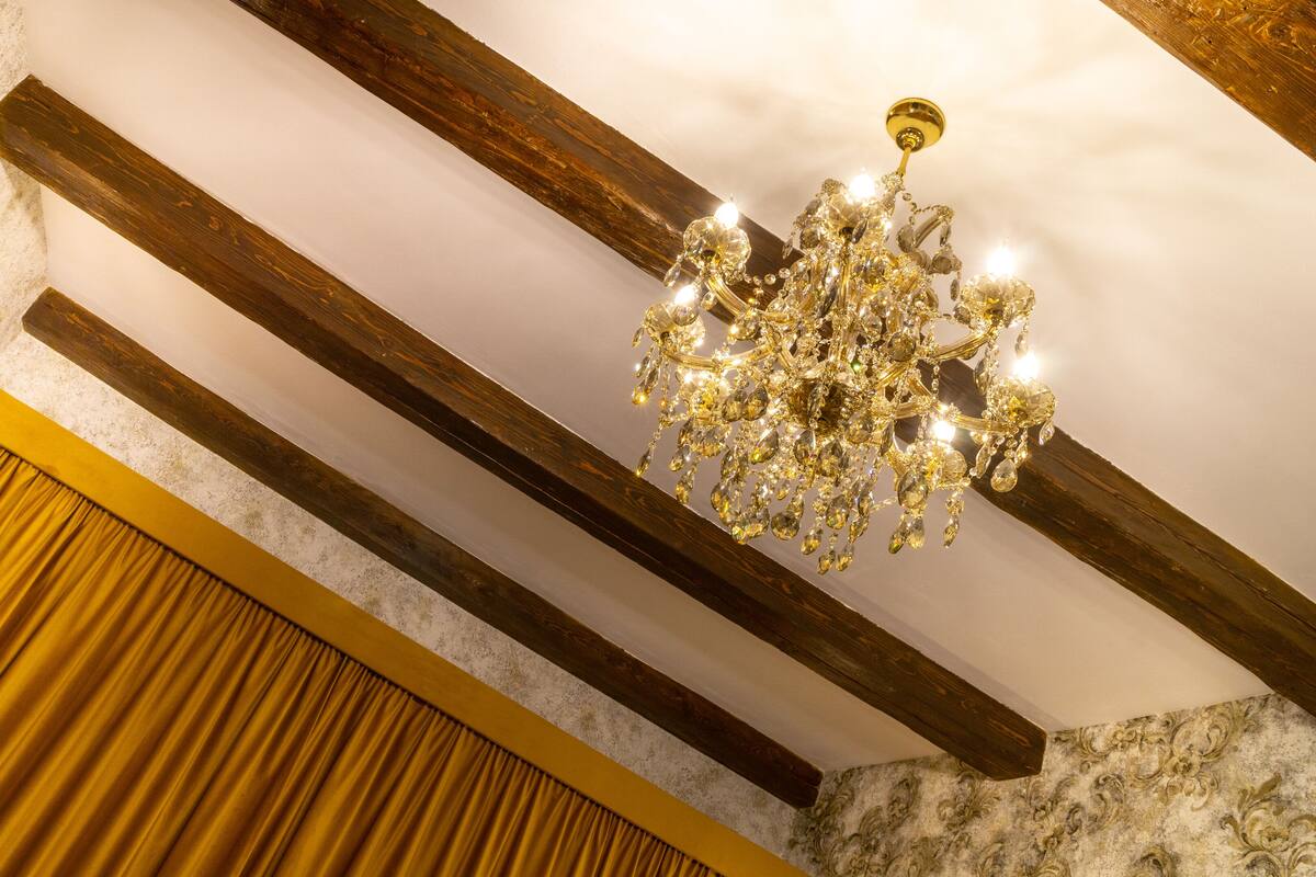 A chandelier with multiple lights and crystals, wooden beams, and a patterned wall.
