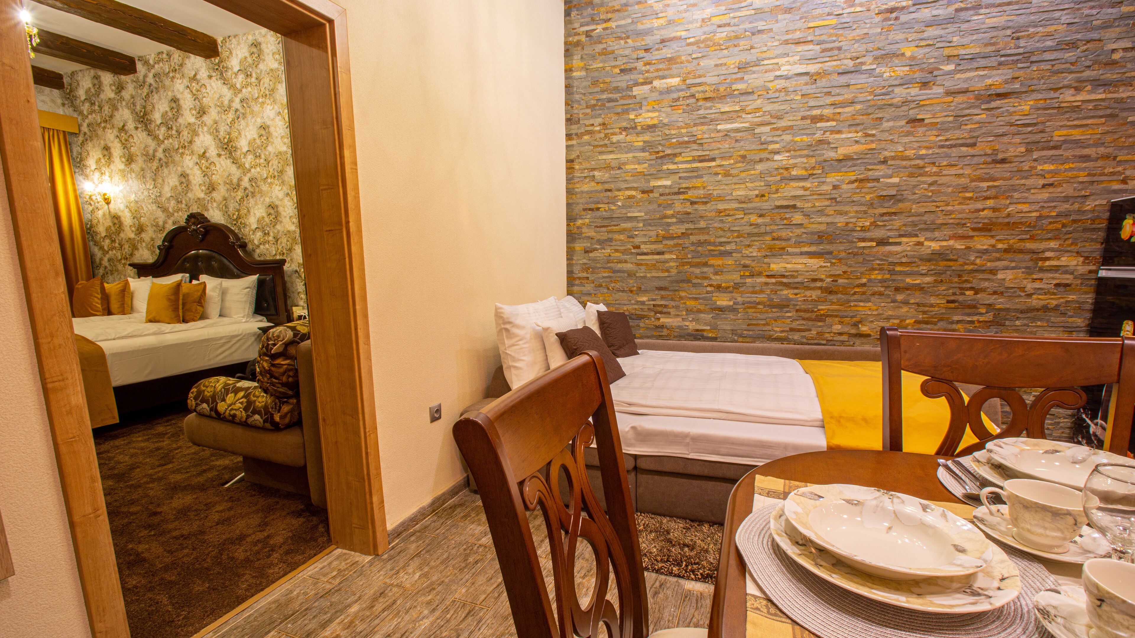 A hotel room with a bed, a dining table set with plates and glasses, and a stone wall.