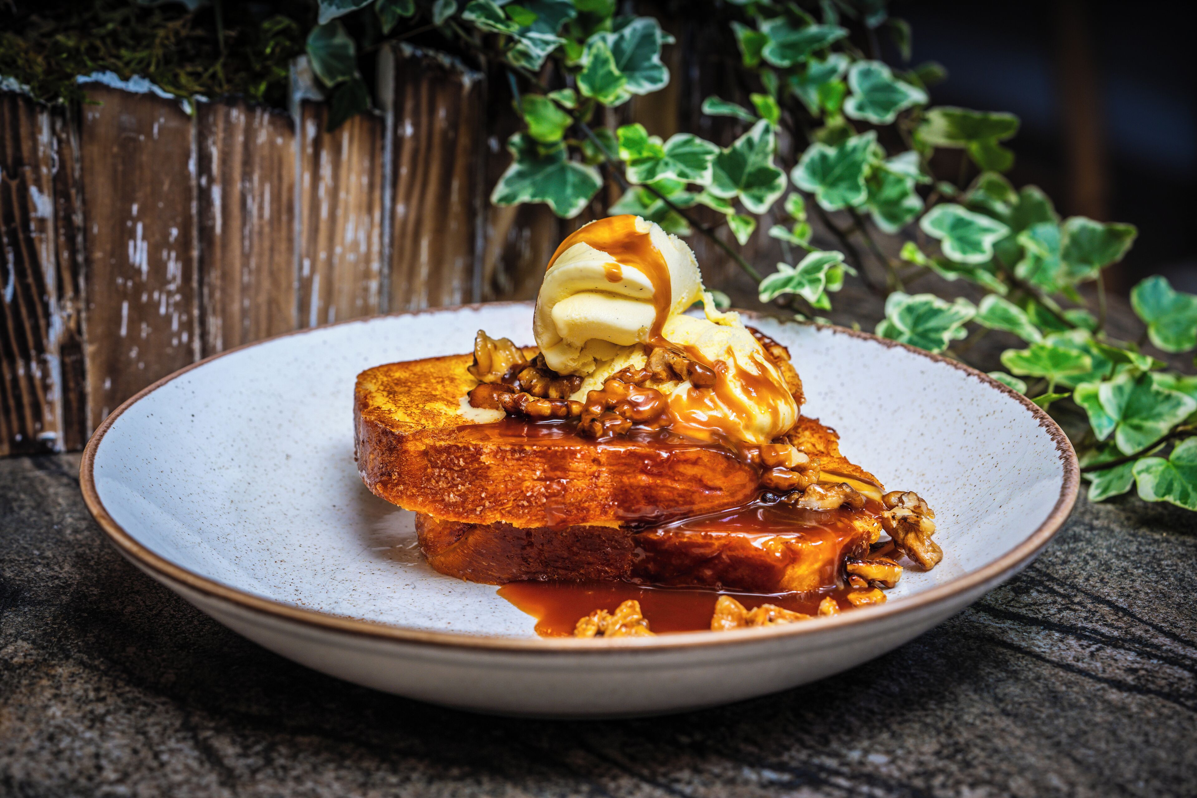 Une assiette de pain perdu nappé de sauce au caramel, accompagnée d’une boule de glace à la vanille.