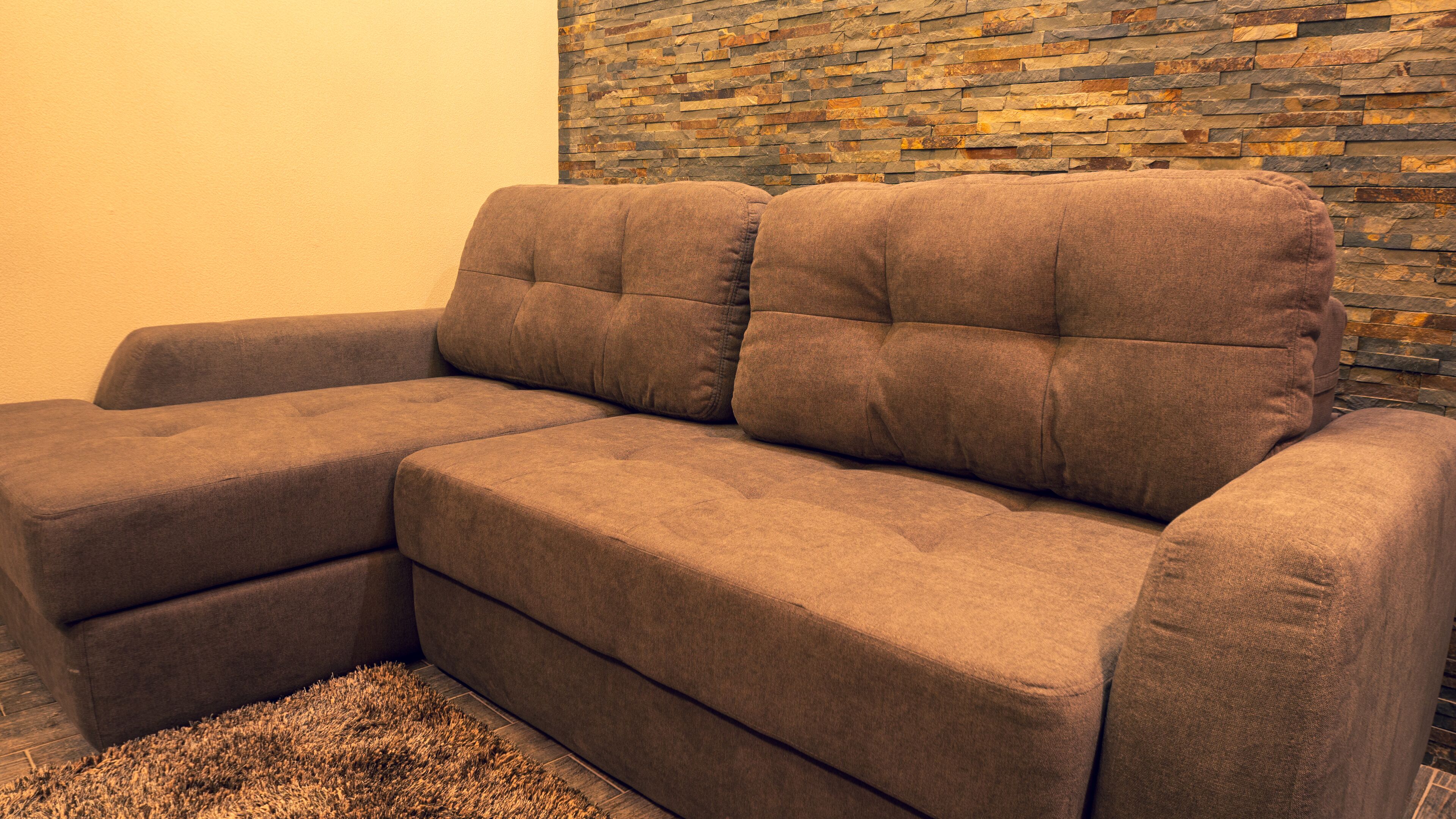 A sectional sofa with a stone wall behind it.