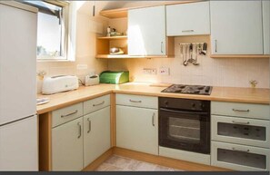 Compact kitchen with oven, microwave, toaster, and additional appliance, featuring light cabinetry and countertop.