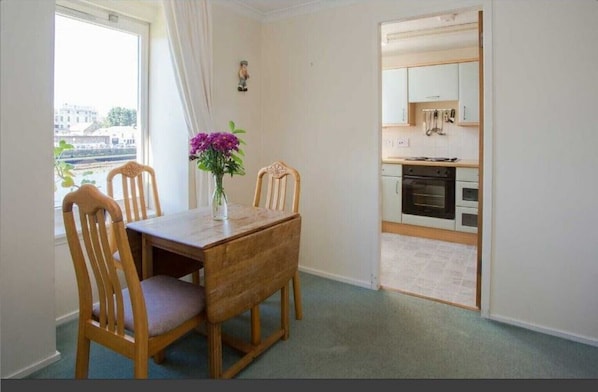A dining area with a wooden table and chairs, a vase with flowers, and a view of the city through a window.