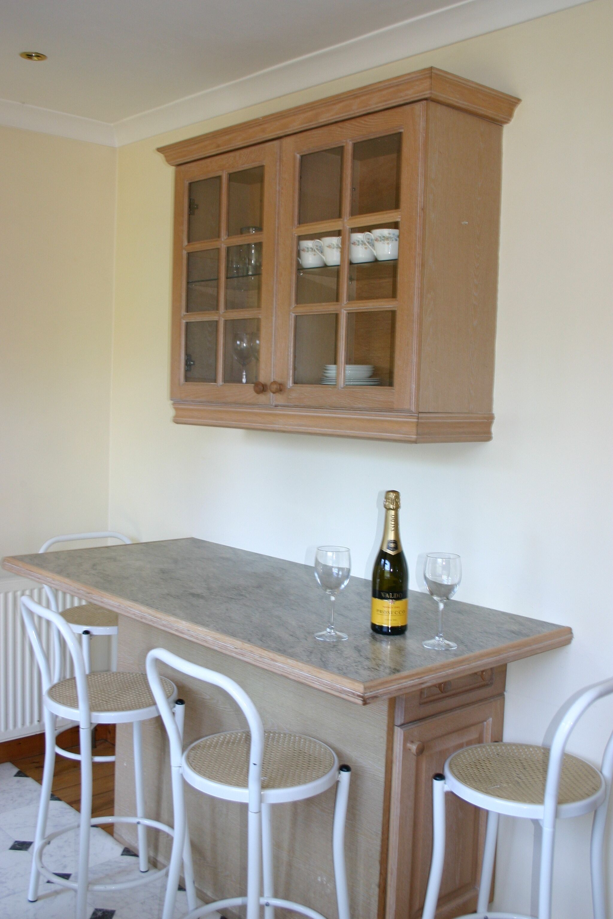 A kitchen with a wooden cabinet, a marble countertop, and three white chairs.