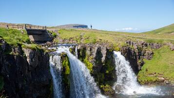 Une cascade se déversant sur un terrain rocheux, avec un pont et une colline au loin.