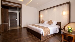 A modern hotel room with a large bed, a wooden headboard, a small table with a vase, and a staircase leading to another room. - Liverpool Hotels, Outer Ring Road, Marathahalli (Bengaluru)