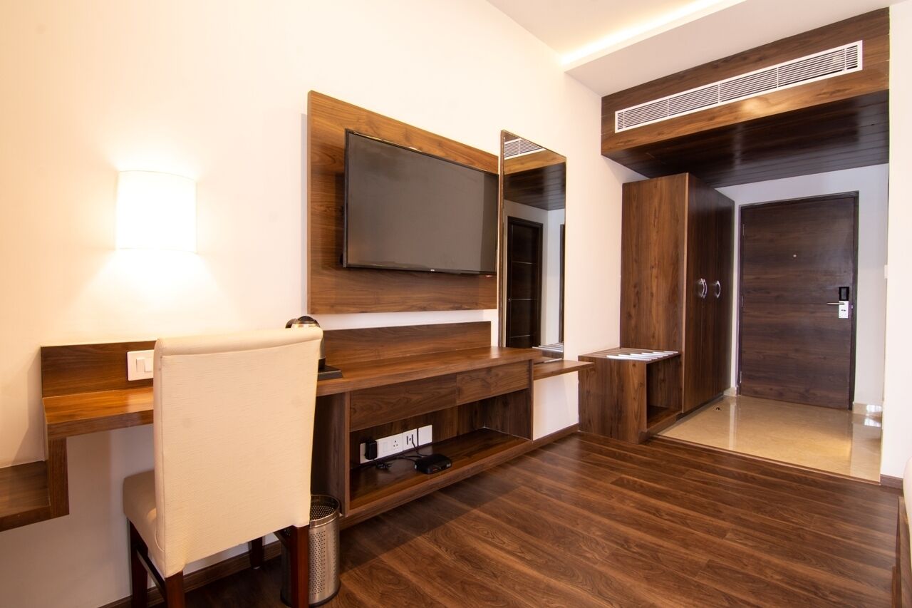 Une chambre d’hôtel moderne avec une console en bois, un téléviseur à écran plat fixé au mur, un miroir et une porte donnant sur un placard.