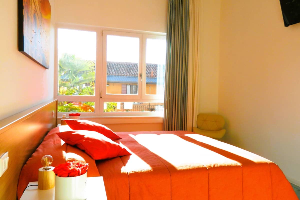 A bedroom with a bed, a bedside table, a lamp, and a window with curtains.