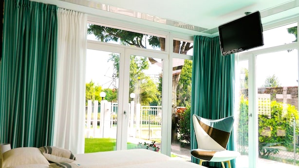 A bedroom with a large bed, a TV mounted on the wall, and a view of the garden through the sliding glass door. - Villa Marina (Venice)