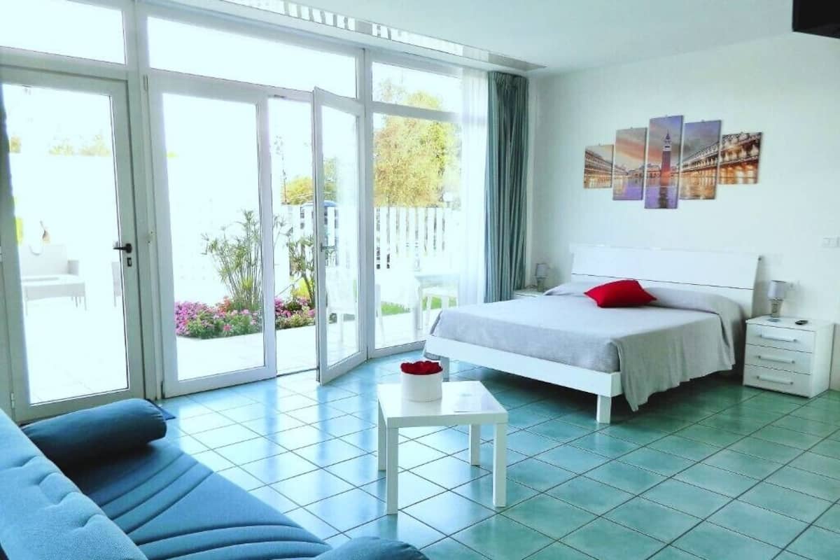 A bedroom with a bed, a nightstand, a small table, and a sofa.