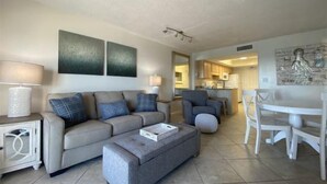 A living room with a sofa, ottoman, and a dining area with a table and chairs. - Flash Sale! Surfside Shores 2/2 Sleeps 8 (Gulf Shores)