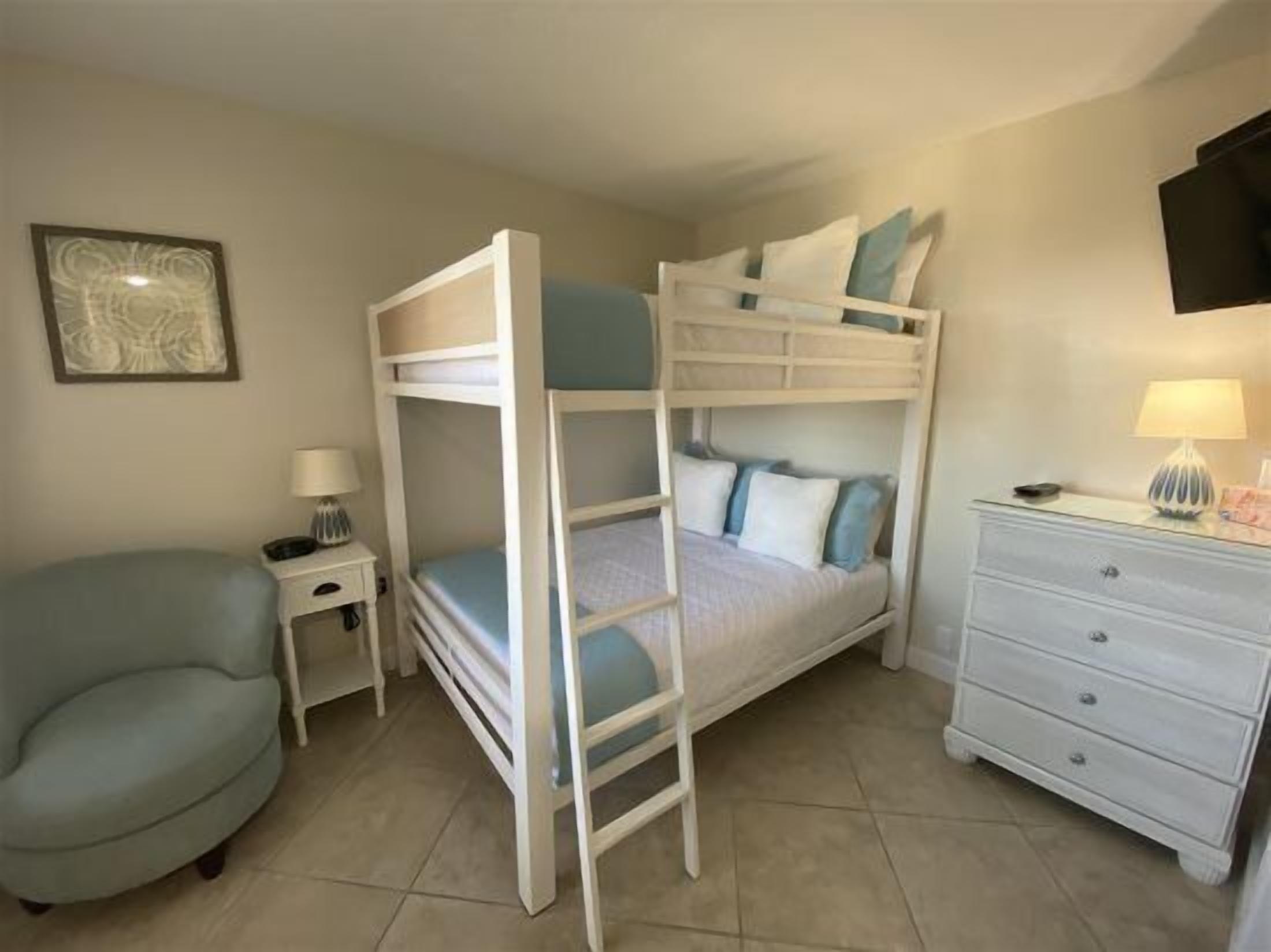 A bunk bed room with a nightstand, a lamp, a chair, and a dresser.