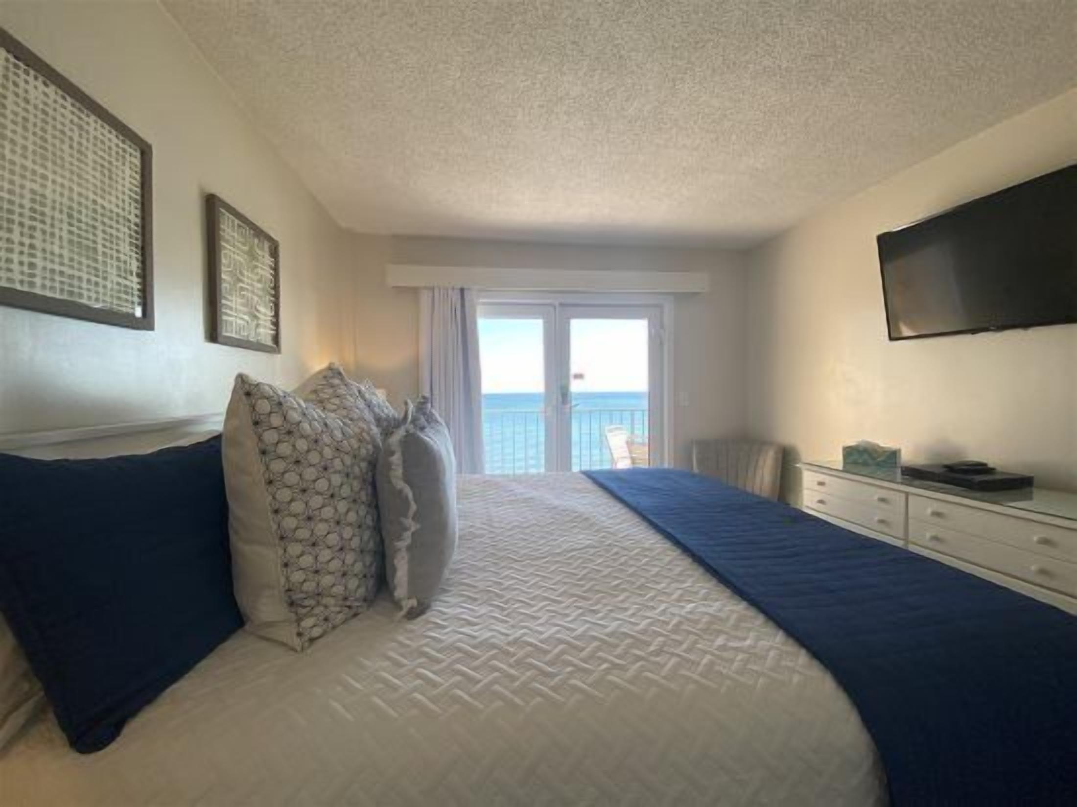 Un dormitorio con cama, televisión y balcón con vistas al mar.