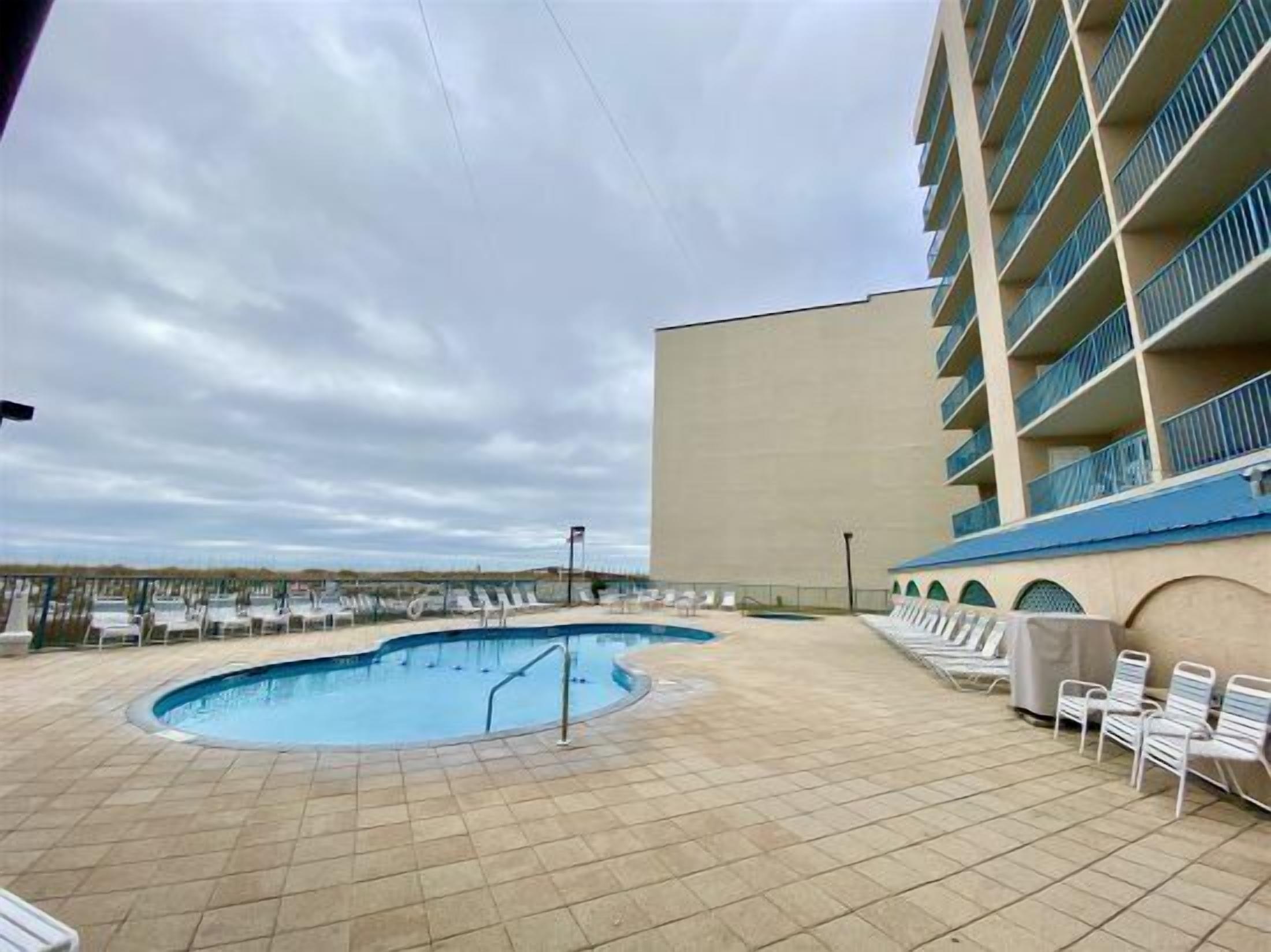 A swimming pool with lounge chairs and a building with balconies.